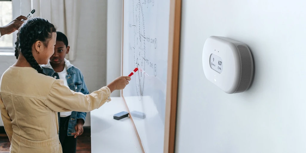 Airthings Space Pro mounted on the wall of a classroom while a student writes on a whiteboard.