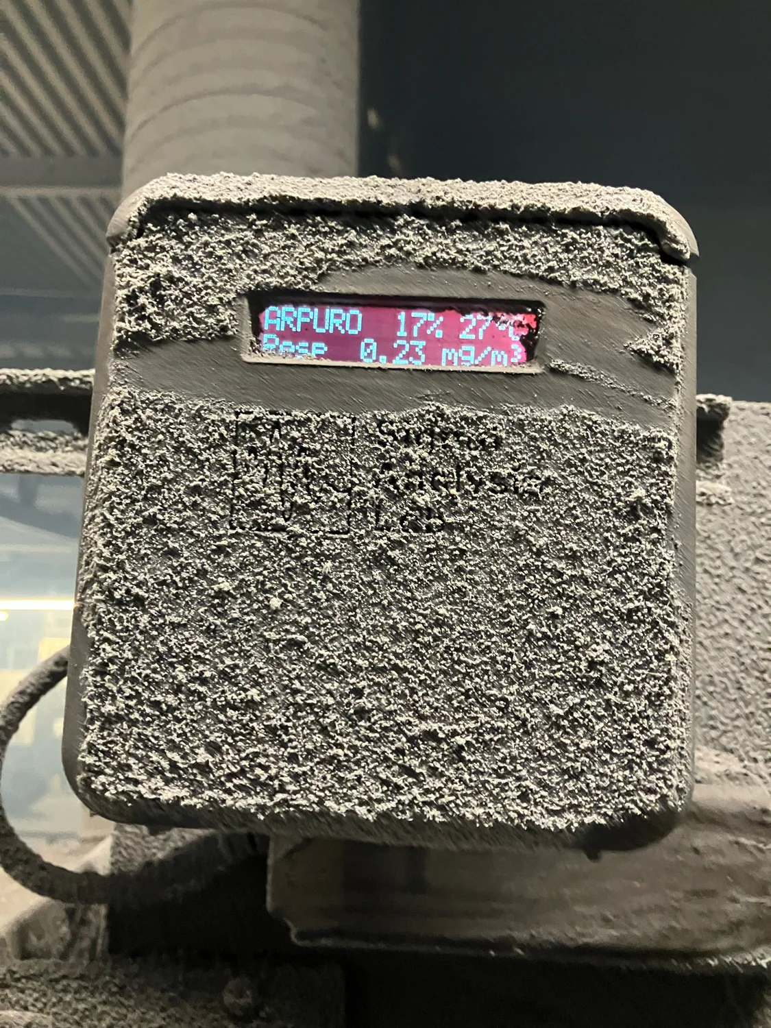 Arpuro sensor in operation, encrusted in industrial dust, with lit display showing a live mg/m³ reading.